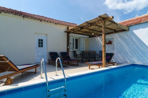 Un área de piscina con sillones de descanso, una pérgola y una pequeña mesa.