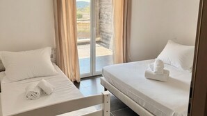 Habitación de hotel con dos camas, una puerta corrediza de vidrio al exterior y un ventilador de techo.