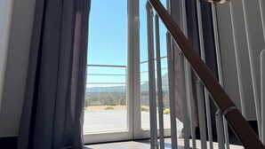 Una escalera con barandilla de madera que lleva a una puerta con vistas a una carretera y colinas.