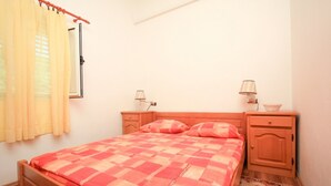 A bedroom with a wooden bed, two bedside tables, a nightstand, a lamp, and a window with curtains. - Apartments Ereš Zuronja-One-Bedroom Apartment with Sea View 2 (Putnikovici)