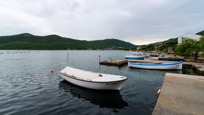 A calm lake with boats docked at a pier, surrounded by hills and a small town. - Apartments Ereš Zuronja-One-Bedroom Apartment with Sea View 2 (Putnikovici)