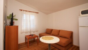 A small living room with a sofa, a small table with a lamp, a TV, and a plant. - Apartments Ereš Zuronja-One-Bedroom Apartment with Sea View 2 (Putnikovici)