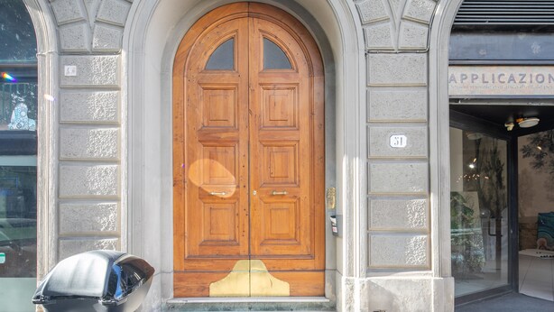 A large wooden double door with a small window above it, set in a stone building with a sign above the door. - Santa Maria Novella 4 Bedrooms by Mmega (Florence)