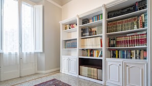 A library with white bookshelves filled with books, a patterned rug on the floor, and a white door with a window. - Santa Maria Novella 4 Bedrooms by Mmega (Florence)