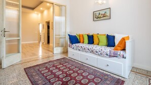 A room with a white sofa bed, colorful pillows, a patterned rug, and a painting on the wall. - Santa Maria Novella 4 Bedrooms by Mmega (Florence)