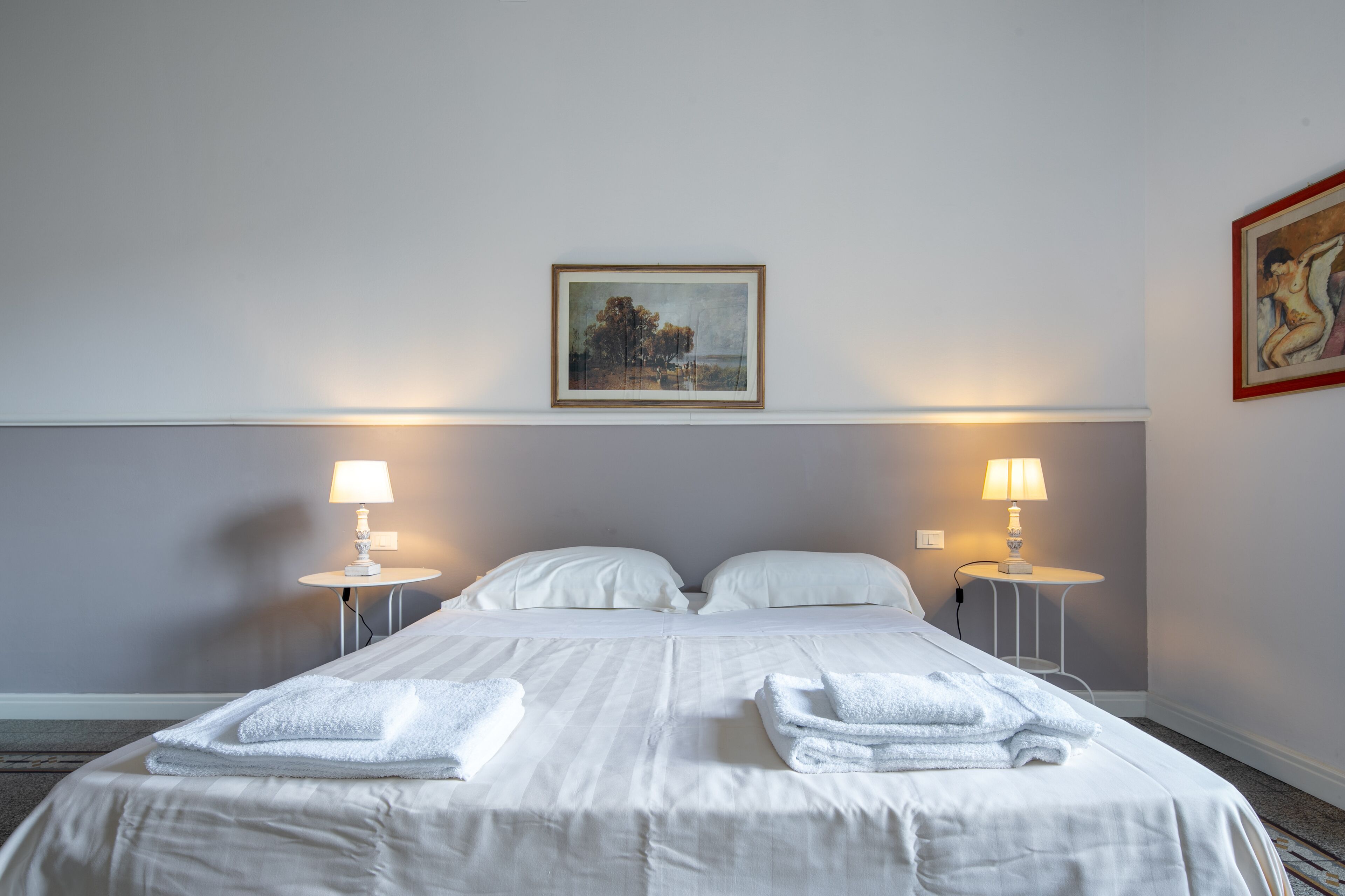 A hotel room with a large bed, two bedside lamps, a painting on the wall, and a small table with a lamp.