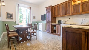 A kitchen with wooden cabinets, a dining table with chairs, a microwave, and a window with shutters. - Santa Maria Novella 4 Bedrooms by Mmega (Florence)