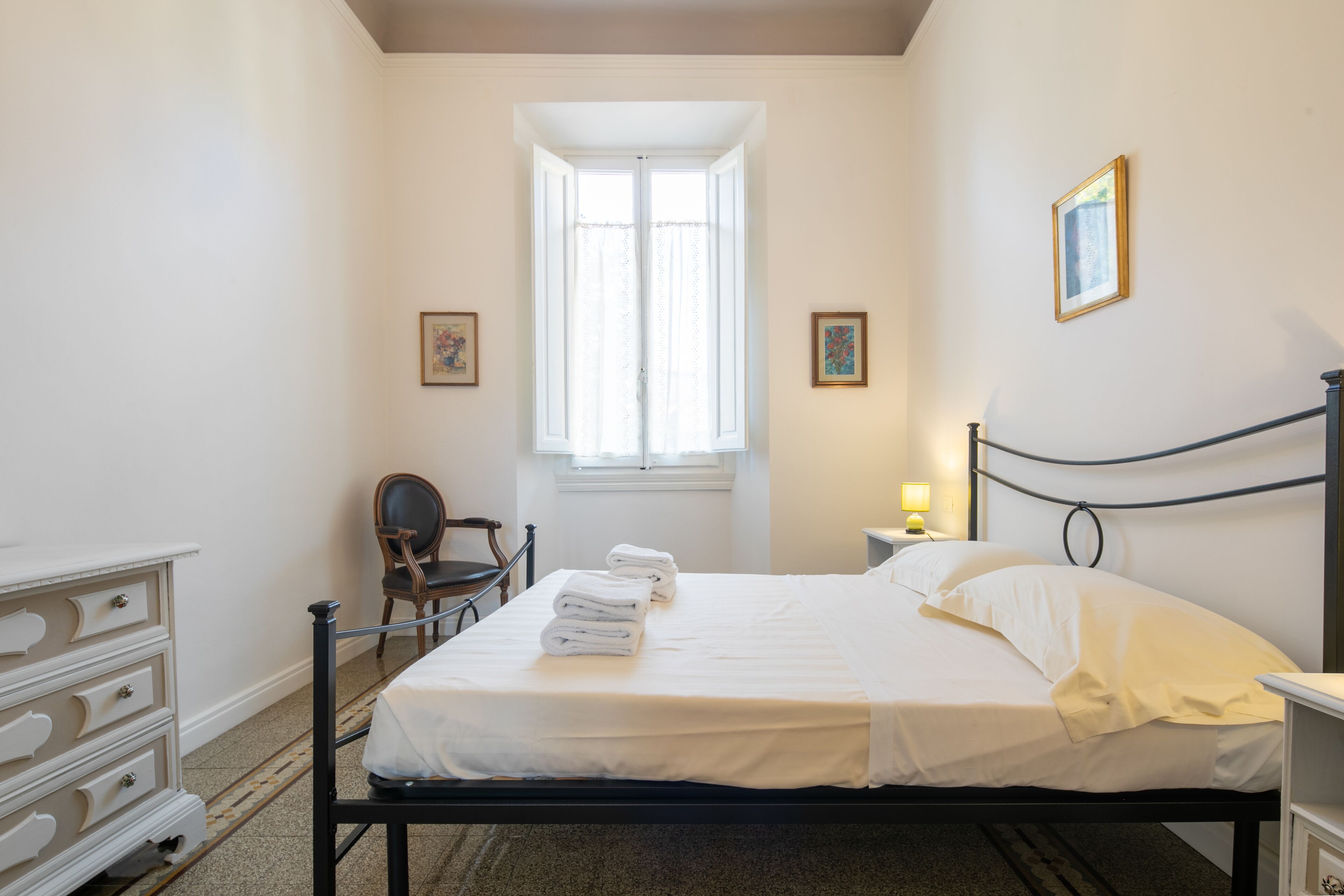 A neatly arranged bedroom with a bed, a dresser, a chair, and a window.