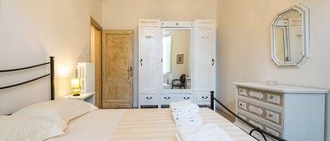 Habitación de hotel con cama, mesita de noche con lámpara, armario y cómoda.