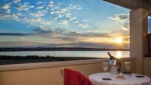 A table with a bottle and glasses, a red towel, and a view of a sunset over water. - Paya II / 2 (Formentera)