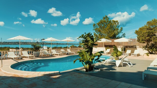 A pool area with lounge chairs, umbrellas, and a view of the sea. - Paya II / 2 (Formentera)