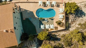 An aerial view of a swimming pool surrounded by lounge chairs and umbrellas, with a building adjacent to the pool area. - Paya II / 2 (Formentera)