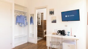 A hotel room with a white wardrobe, a desk with a chair, a small fridge, a TV, and a shower area. - Mapi's rooms (Cagliari)
