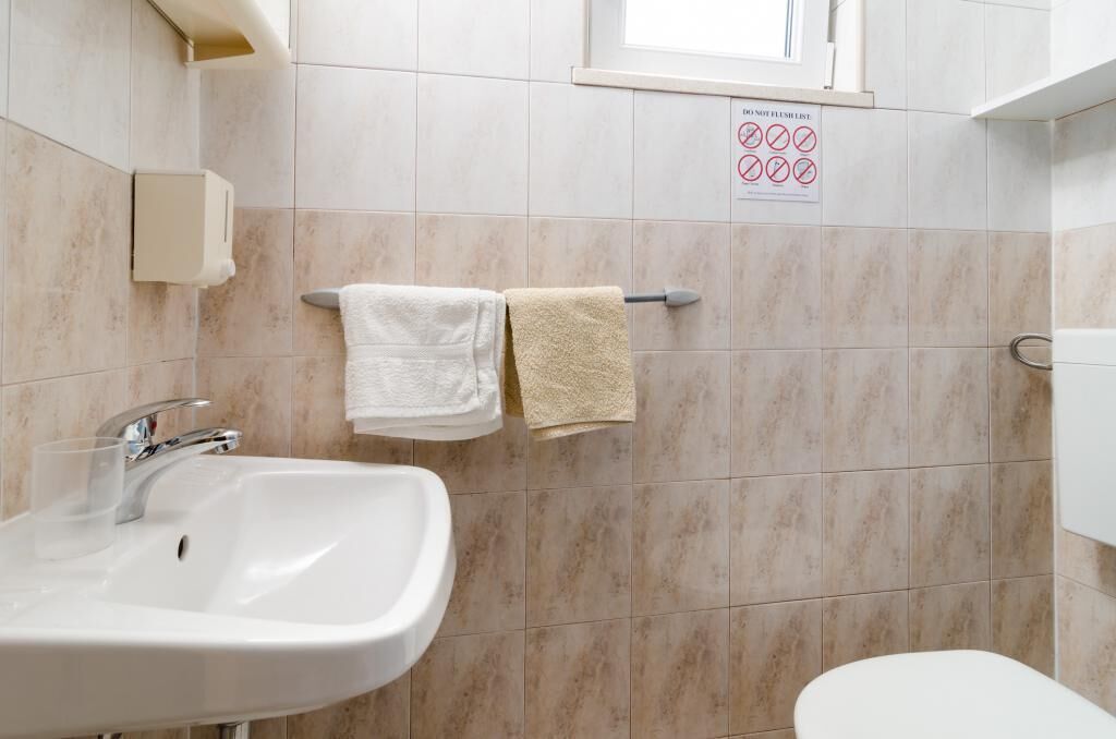 A bathroom with a white sink, two towels, and a sign indicating no flushing.