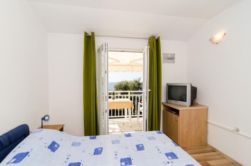 A bedroom with a bed, a television on a wooden cabinet, and a balcony with a table and chairs.