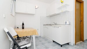 Una cocina compacta con armarios blancos, una mesa de comedor con una botella y un vaso, y una silla con un cojín estampado.