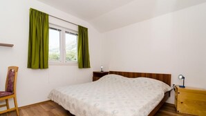 Ein Schlafzimmer mit einem hölzernen Bett, grünen Vorhängen, einem Nachttisch aus Holz, einem Stuhl und einem Fenster mit Blick ins Grüne.