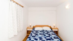 Ein Schlafzimmer mit einem hölzernen Bett, weißen Vorhängen, zwei Nachttischen mit Lampen und einer schlichten weißen Wand.