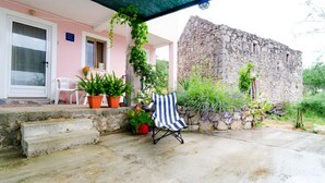 Eine überdachte Terrasse mit Steinmauer, Blumentöpfen und einem Streifenstuhl.