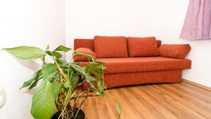 Ein Zimmer mit einem roten Sofa, einer großen grünen Pflanze und einem Holzboden.