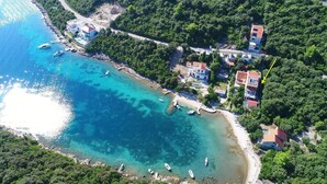An aerial view of a coastal area with clear turquoise waters, boats, and a mix of residential buildings. - Apartments Villa Cebalo Kor (Korcula)
