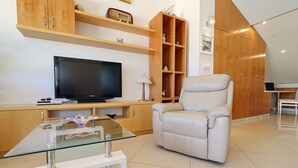 A modern living room with a flat-screen TV, a glass coffee table, a white leather sofa, wooden shelving with decorative items, and a wooden cabinet. - Apartments Villa Cebalo Kor (Korcula)