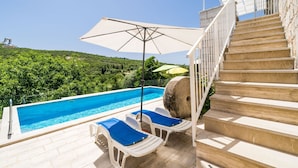 Ein Poolbereich mit freiem Blick auf die umliegende Landschaft, eine Treppe und ein großer Sonnenschirm, der Schatten spendet.