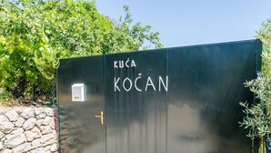 Ein schwarzes Metalldrahtgitter mit der Aufschrift 'KUČA KOČAN' und eine kleine weiße Kiste auf der linken Seite.