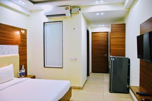 A hotel room with a bed, a refrigerator, a TV, and a door leading to another room. - When In Gurgaon - Service Apartments, Opp Artemis Hospital (Gurugram)