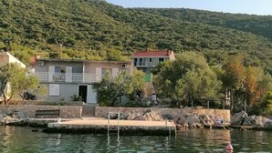 Un bâtiment situé sur la côte, doté d’un quai, et entouré de verdure et de collines.