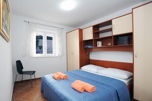 A bedroom with a bed, a chair, a window, and built-in storage cabinets.