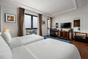 A hotel room with two large beds, a desk with a chair, a television, and a city view. - The Q Hotel Hanoi (Hanoi)