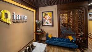 A well-lit reception area with a blue sofa, a small table with decorative items, and a wall with a 'Qiana Wellness and Spa' sign. - The Q Hotel Hanoi (Hanoi)
