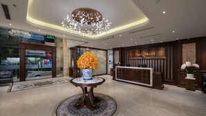 A hotel lobby with a reception desk, a large vase with flowers, and a chandelier. - The Q Hotel Hanoi (Hanoi)