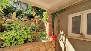 Un petit jardin clos, avec un mur en pierre, des plantes en pot et une fenêtre.