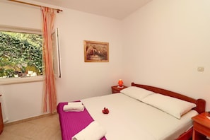 Una camera d'albergo con un letto, un comodino, una finestra con tende e un quadro appeso al muro.