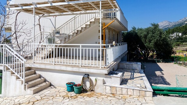 A two-story building with a white exterior, a covered outdoor area with a pergola, and a stone-paved entrance.