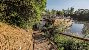 A wooden staircase leading to a boat with a wooden deck and railings, surrounded by greenery and a calm river. - Prague Bay Houseboats (Prague)