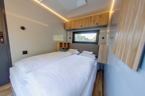 A modern bedroom with a large bed, wooden headboard, built-in shelves, and a window providing natural light.