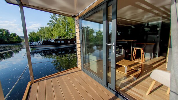 A modern boat interior with a wooden deck, glass sliding doors, and a dining area with a table and chairs. - Prague Bay Houseboats (Prague)