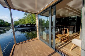 A modern boat interior with a wooden deck, glass sliding doors, and a dining area with a table and chairs.