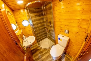 A wooden cabin bathroom with a glass shower enclosure, a sink, and a toilet.
