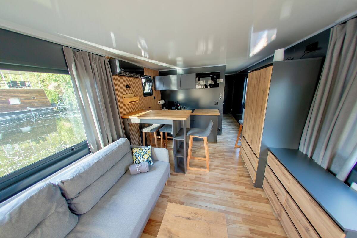 Un interior de autocaravana moderna con sofá, mesa de comedor, zona de cocina y ventanas amplias.