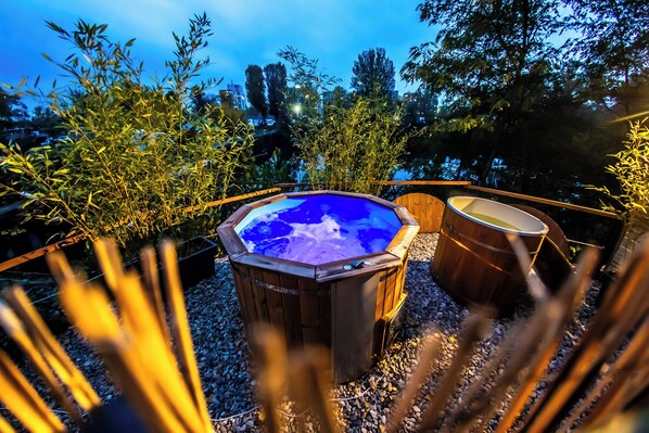 A hot tub with a wooden exterior and a glass top, surrounded by gravel and bamboo plants. - Prague Bay Houseboats (Prague)