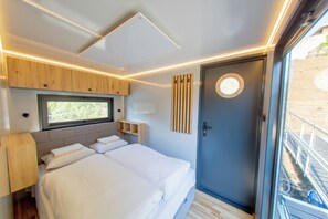 A modern bedroom with a bed, a window, and a door. - Prague Bay Houseboats (Prague)