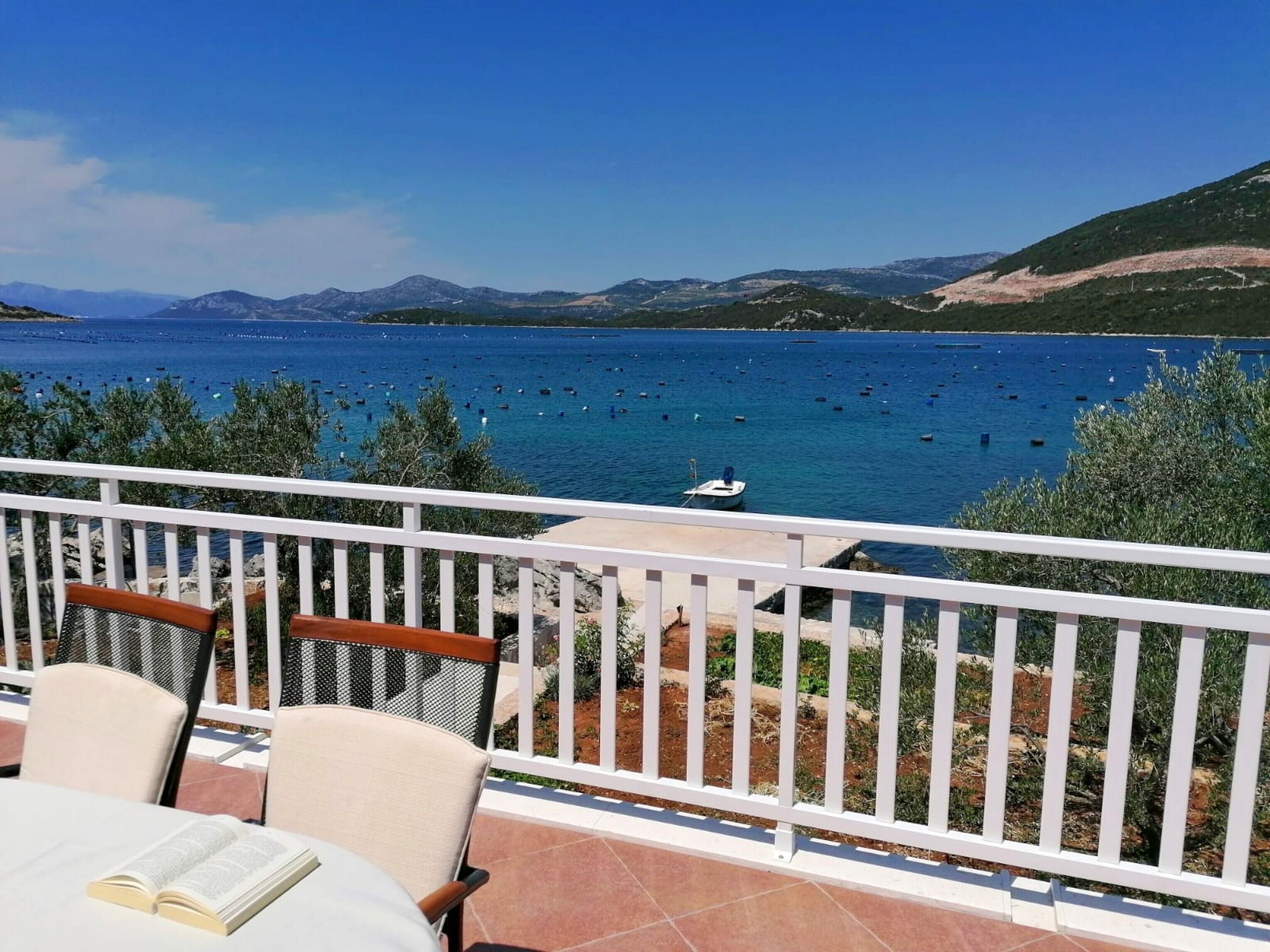 A terrace with a view of the sea, chairs, and a table with an open book.