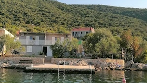 A coastal building with a red roof, situated by a calm body of water with a dock.