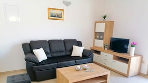 A modern living room with a black leather sofa, a wooden coffee table, a TV on a wooden stand, and a small potted plant.