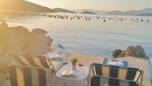 A beachside seating area with a table, chairs, and a view of the sea and distant mountains.