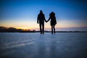 Two people holding hands on a frozen surface with a sunset in the background.